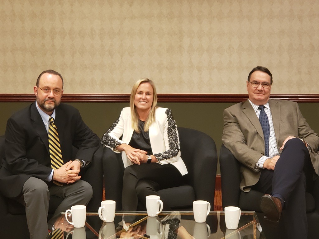Three professionals seated together in a conference setting, including Ashley Kelm, President of ISI, participating in a business discussion with two male colleagues.