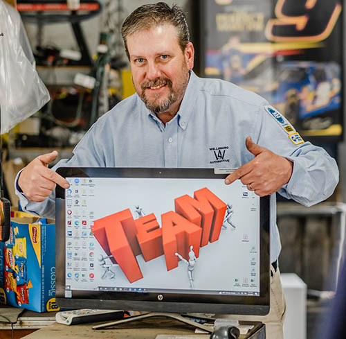 Workshop professional pointing at a desktop monitor showing a “TEAM” teamwork graphic, representing collaboration, leadership, and problem solving in a technical environment.
