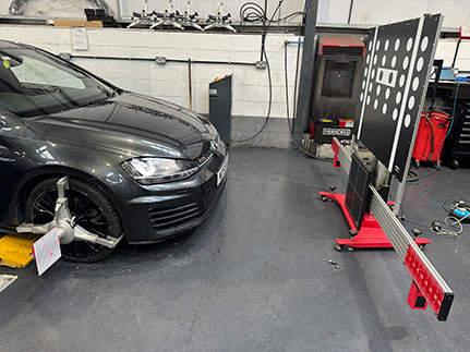 Vehicle undergoing wheel alignment service in an automotive repair workshop with alignment equipment.